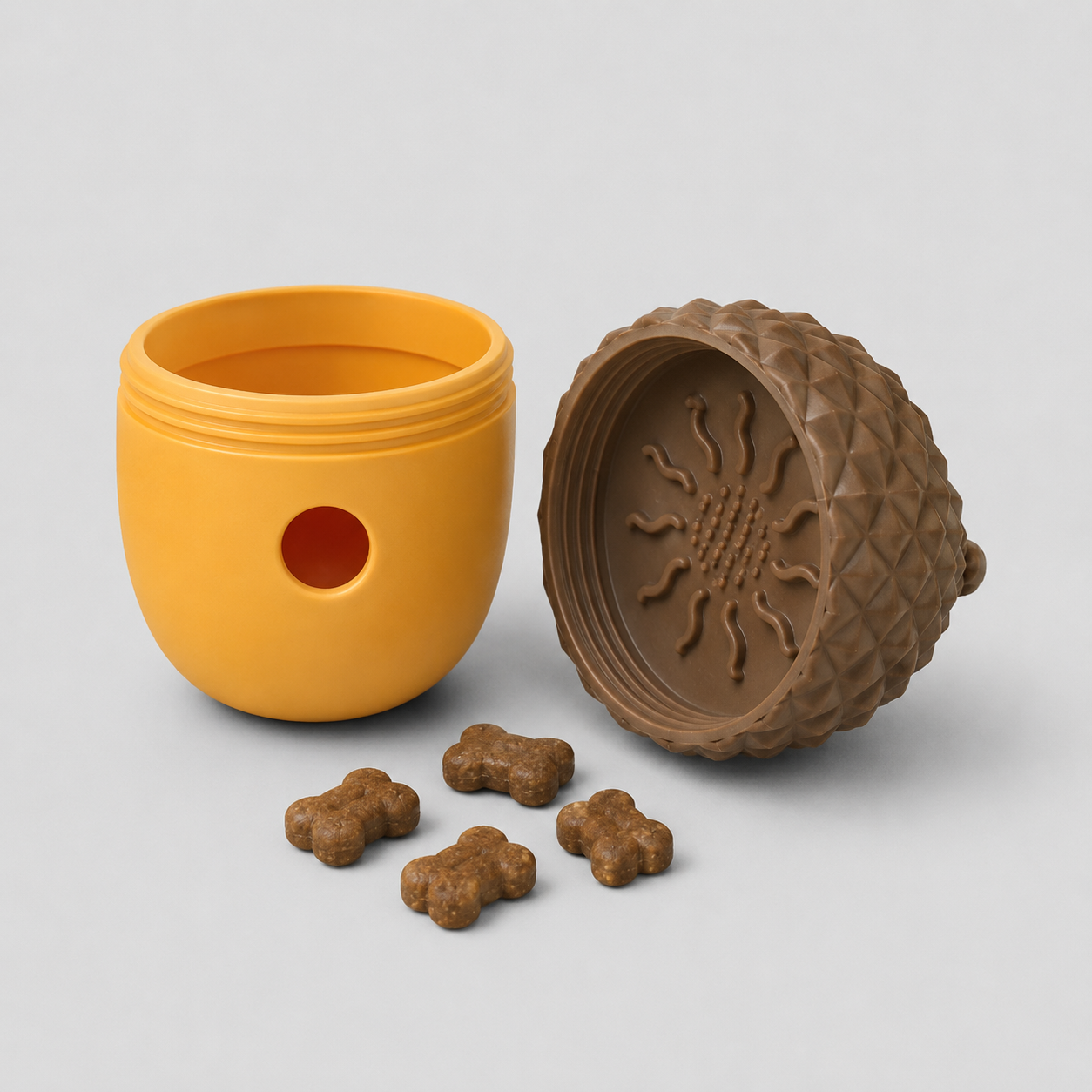 Yellow acorn dog toy with a brown lid featuring a scorpion design, accompanied by brown dog treats on a light grey background.