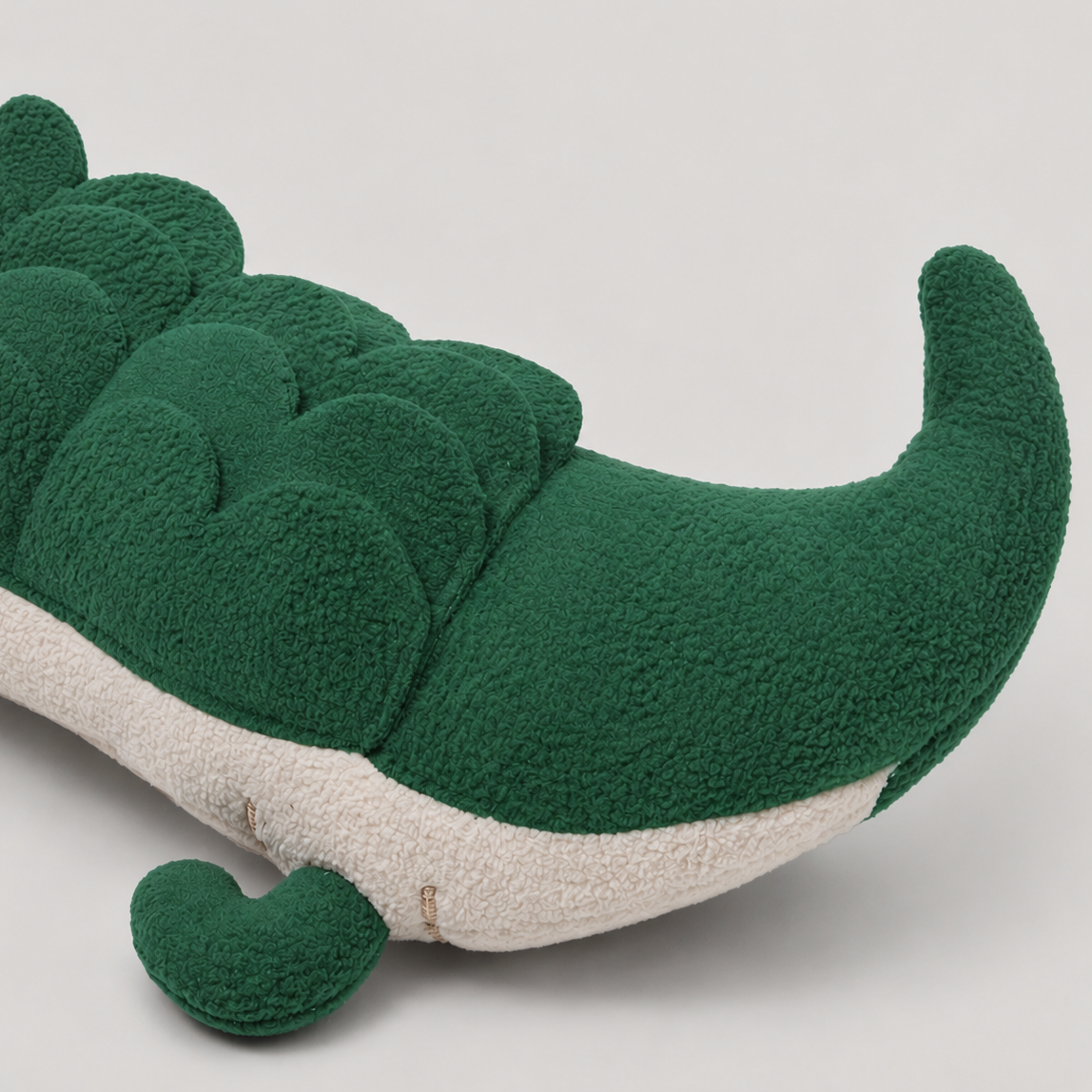 Green plush dog toy crocodile tail on a light grey background