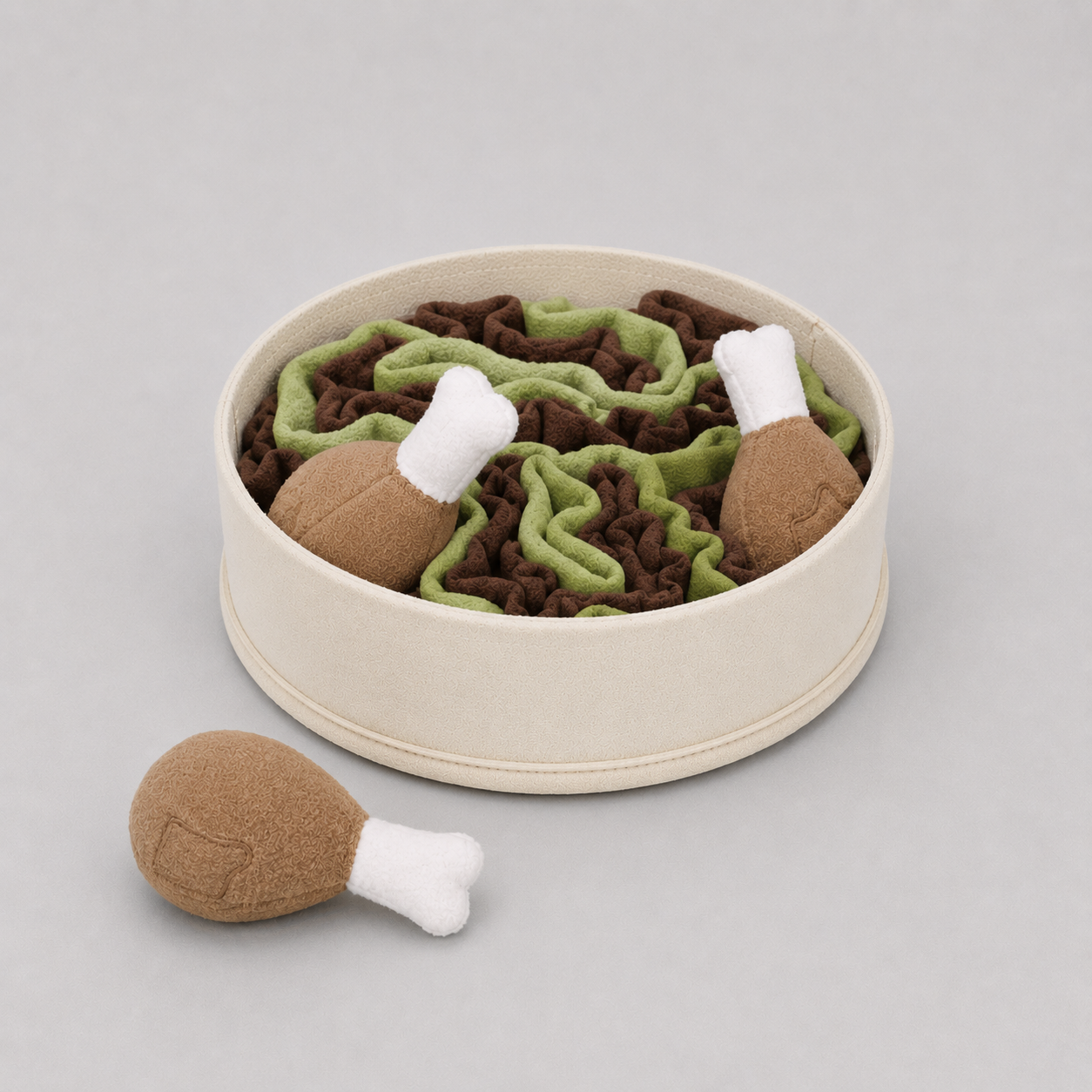 Pet toy set with green and brown pieces resembling grass and leaves, and brown and white pieces resembling chicken legs, in a beige container on a light grey background.