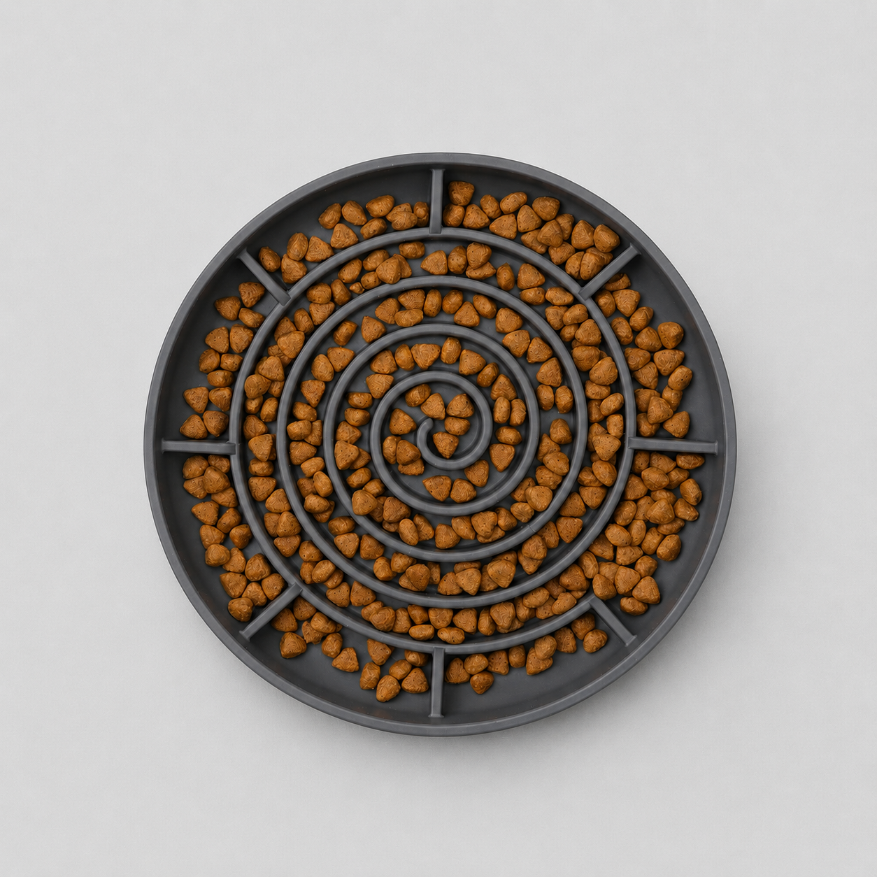 Aerial image of a grey spiral slow feeding dog bowl filled with brown kibble on a light grey background