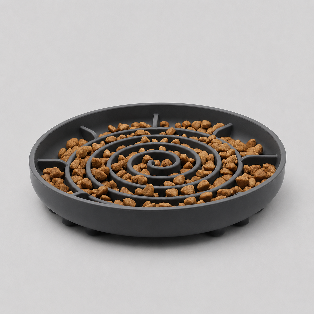 Grey slow feeder dog bowl with a spiral design filled with brown kibble on a light grey background
